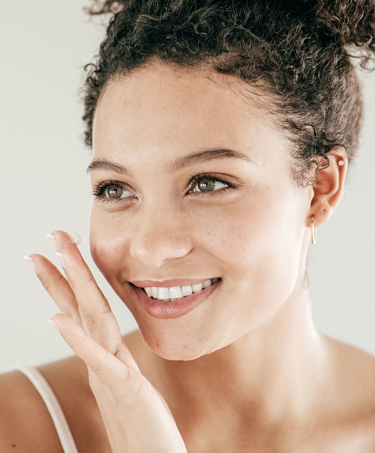 Smiling woman applying skincare product to face.