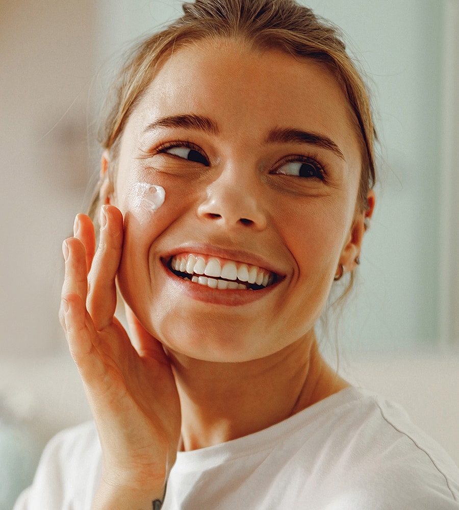 Smiling woman applying moisturizer to her face.